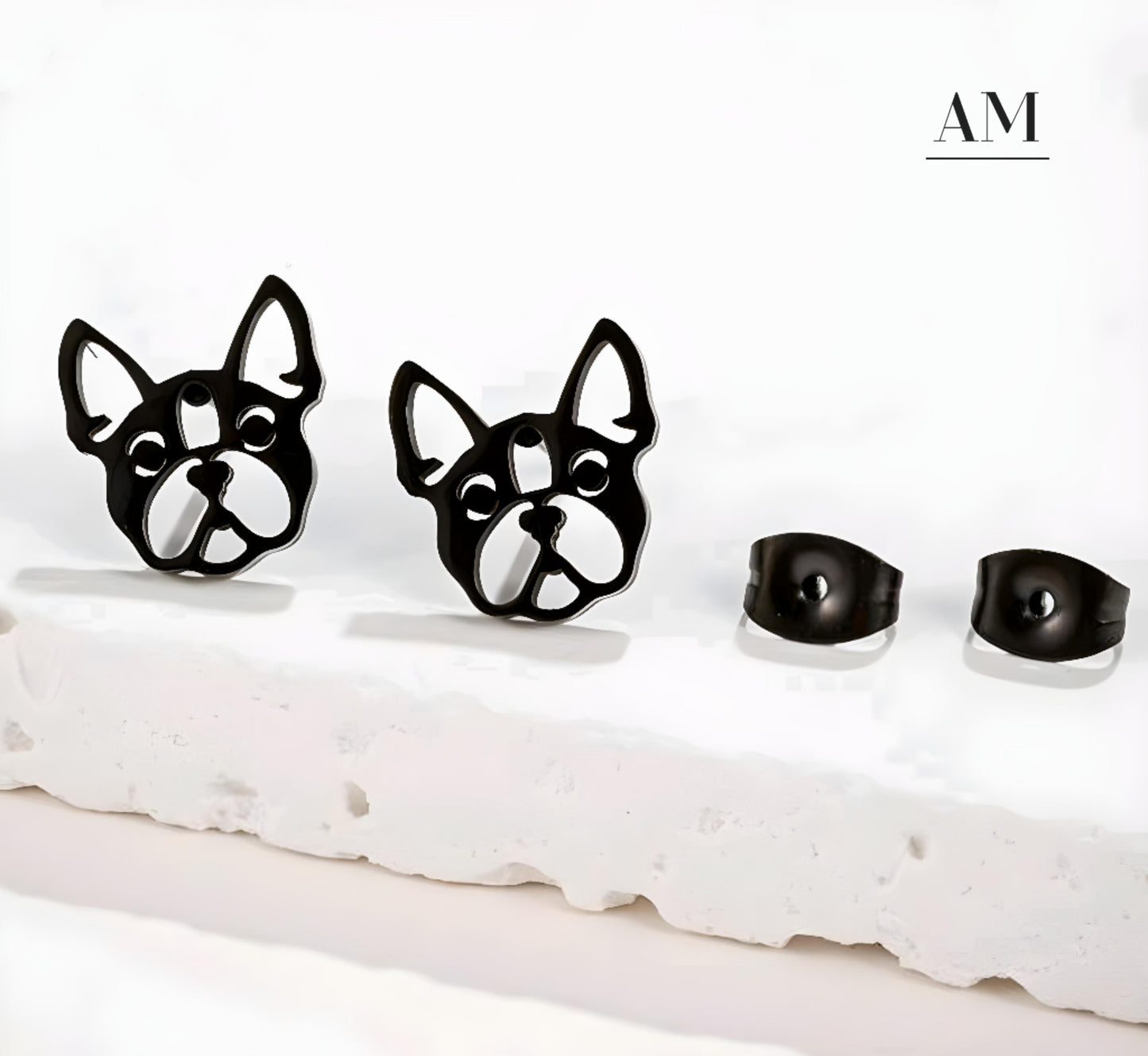 A pair of black stainless steel bulldog earrings displayed on a stand, with the brand name 'AM' visible at the top.