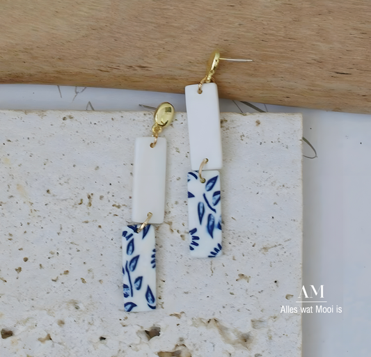 A pair of blue and white leaf pattern earrings with a gold-colored hook, displayed on a white textured surface.
