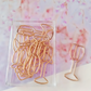 Gold paper clips shaped like wine glasses on a pink floral background
