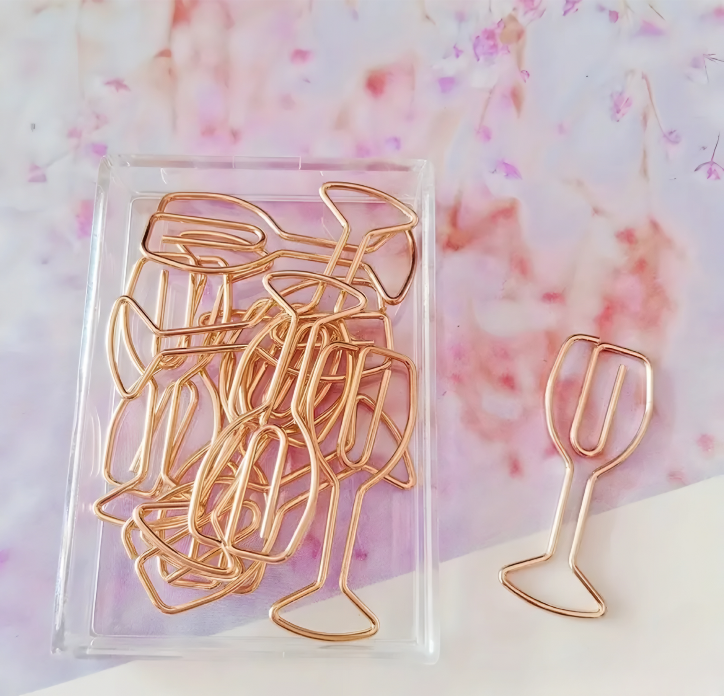 Gold paper clips shaped like wine glasses on a pink floral background